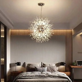 Modern bedroom with a stylish El Sol Crystal Dandelion Lighting Fixture from Morsale.com resembling a burst of light above a neatly made bed with multiple pillows. The room features a wood-paneled accent wall, bedside tables with lamps, and a small desk with a plant on the right. Minimalist and cozy decor.