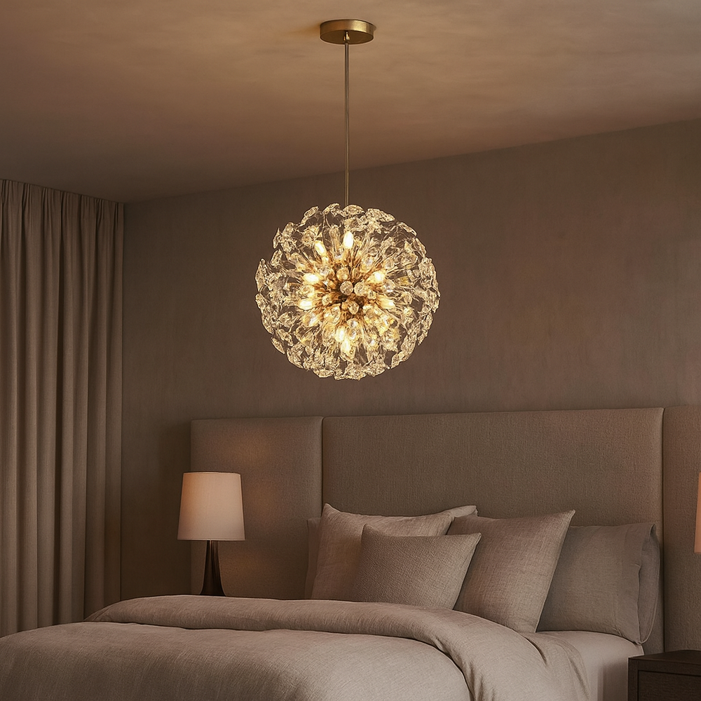 A cozy bedroom with beige walls and bedding features the Aurelio Dandelion Sphere Chandelier from Morsale.com, its glowing, flower-like LEDs suspended above the bed. A bedside table with a lamp sits to the left, and curtains cover a window.