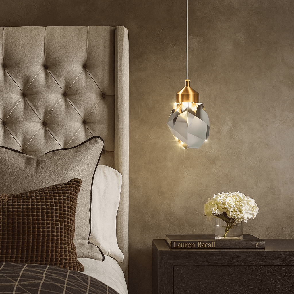 A modern bedroom features a tufted headboard, brown textured pillows, the Morsale Valenza Grand Crystal Pendant for luxurious lighting, a side table with a white flower arrangement, and the book “Lauren Bacall.”.