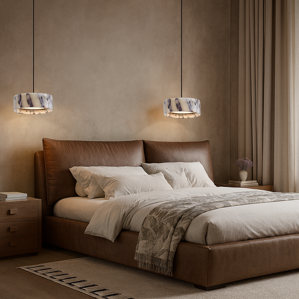 A modern bedroom with a large brown leather bed, white and beige bedding, and Morsale Solara Natural Stone Pendants above the bedside tables. Neutral walls, floor-to-ceiling curtains, and a vase with flowers complete the look.