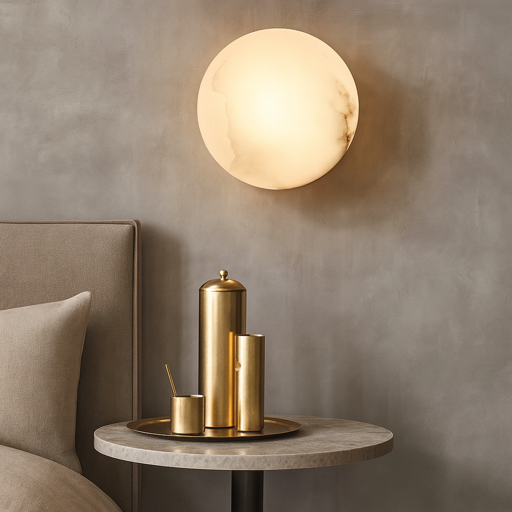 The Morsale Moonshade Marble Ball Light Fixture glows above a gray nightstand holding gold-toned containers and a tray. Nearby, a beige upholstered bed with a matching pillow complements the sleek, minimalist décor.