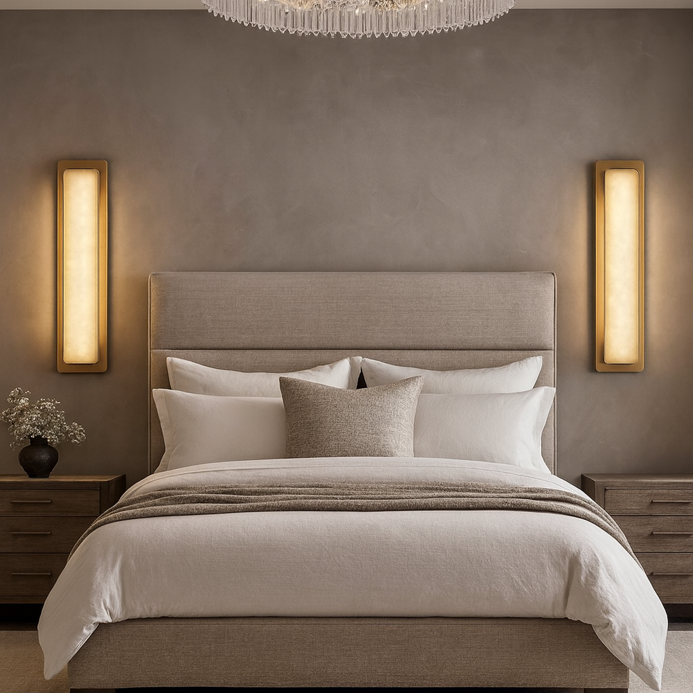 A modern bedroom with a beige upholstered bed, white and beige bedding, wooden nightstands, and a chandelier. Dimmable Capri Marble Wall Sconces by Morsale flank the bed, with a small vase of flowers on one nightstand.