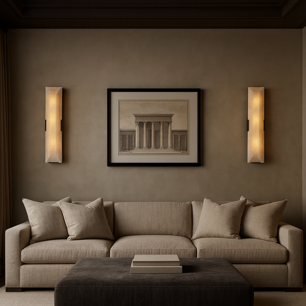
                  
                    A modern living room with a beige sofa, four matching pillows, a large dark ottoman, and two Brookhill Calcite Wall Sconces by Morsale.com. A framed print of a classical building decorates the taupe wall for a minimalist touch.
                  
                