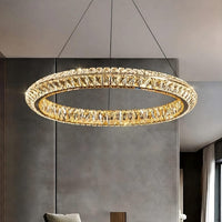 The Bacci Crystal Ring Chandelier by Morsale.com, featuring a gold frame and sparkling crystals, is suspended by thin wires in a minimalist room with gray walls and tall windows.