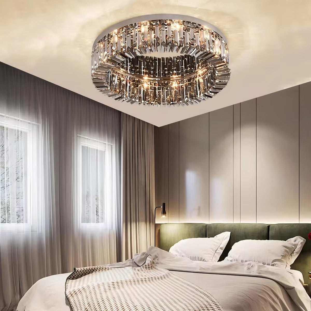 A modern bedroom features a Morsale.com Specchio Smoke Grey Crystal Ceiling Light with clear crystals and E14 LED bulbs, casting a warm glow. The room includes a large bed with white pillows and a houndstooth-patterned throw blanket, situated against a paneled wall. Two windows with sheer curtains allow natural light in.