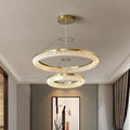 The Morsale.com Bergamo Crystal Chandelier elegantly illuminates a minimalist room with its energy-efficient design, featuring dual gold and clear crystal rings at varied heights. A contemporary artwork adorns the creamy walls, while dark curtains add a touch of elegance to the windows.