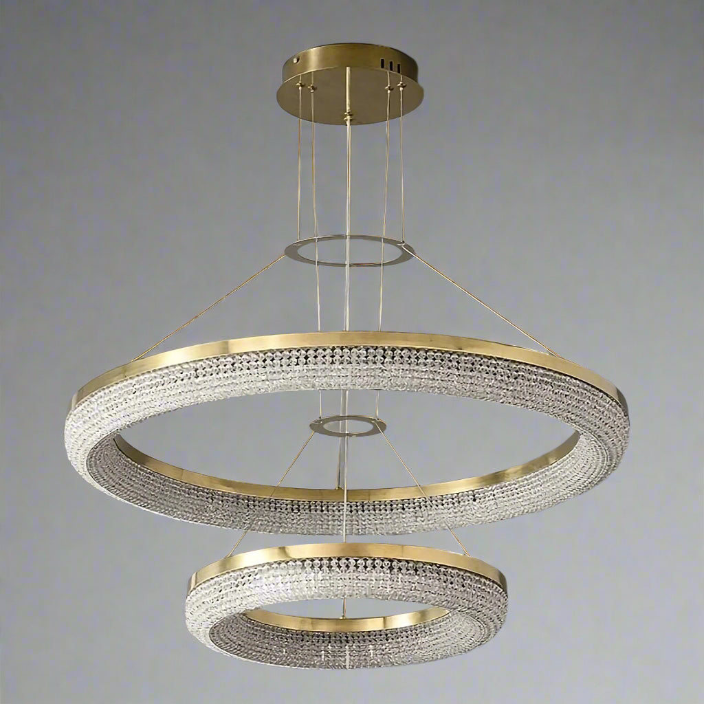 Introducing Morsale.com's Bergamo Crystal Chandelier: a modern masterpiece with two gold rings suspended by wires, adorned with handmade clear crystals. It casts a dazzling effect on gray walls, while providing energy-efficient lighting.