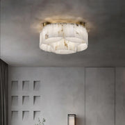 A modern living room with minimalist decor featuring a large Moonshade Natural Marble Ceiling Light Fixture from Morsale.com on the ceiling. The room includes a grey sofa, a tall floor lamp, and a small table with a decorative plant. The walls are textured and light grey, creating an elegant yet simple ambiance.
