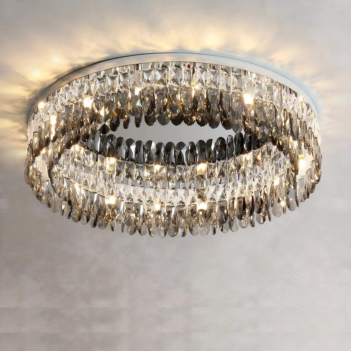A handmade Giano Crystal Ceiling Light by Morsale.com with two concentric rings of hanging crystals, mounted flush to the ceiling. The chandelier is illuminated, creating a sparkling effect as light reflects off the crystals. The plain, light-colored ceiling enhances its classic luxury appeal.