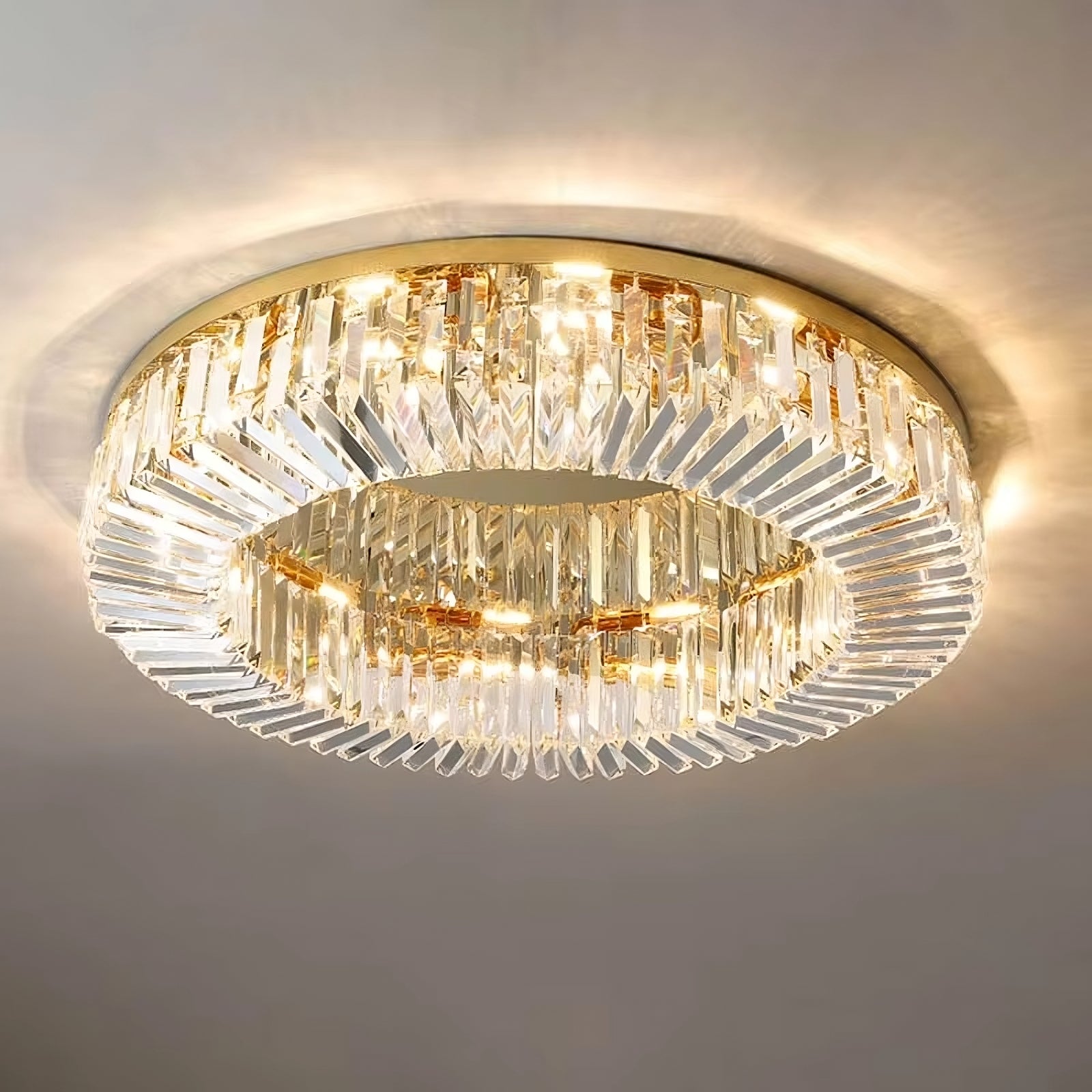 The Morsale.com Gio Crystal Ceiling Light showcases a round, flush-mounted design with an electroplated finish, enhanced by two tiers of clear, vertical crystal prisms that beautifully refract light. Featuring energy-efficient E14 LED bulbs and a gold base, it emits a warm, ambient glow for a sophisticated and luxurious aesthetic.