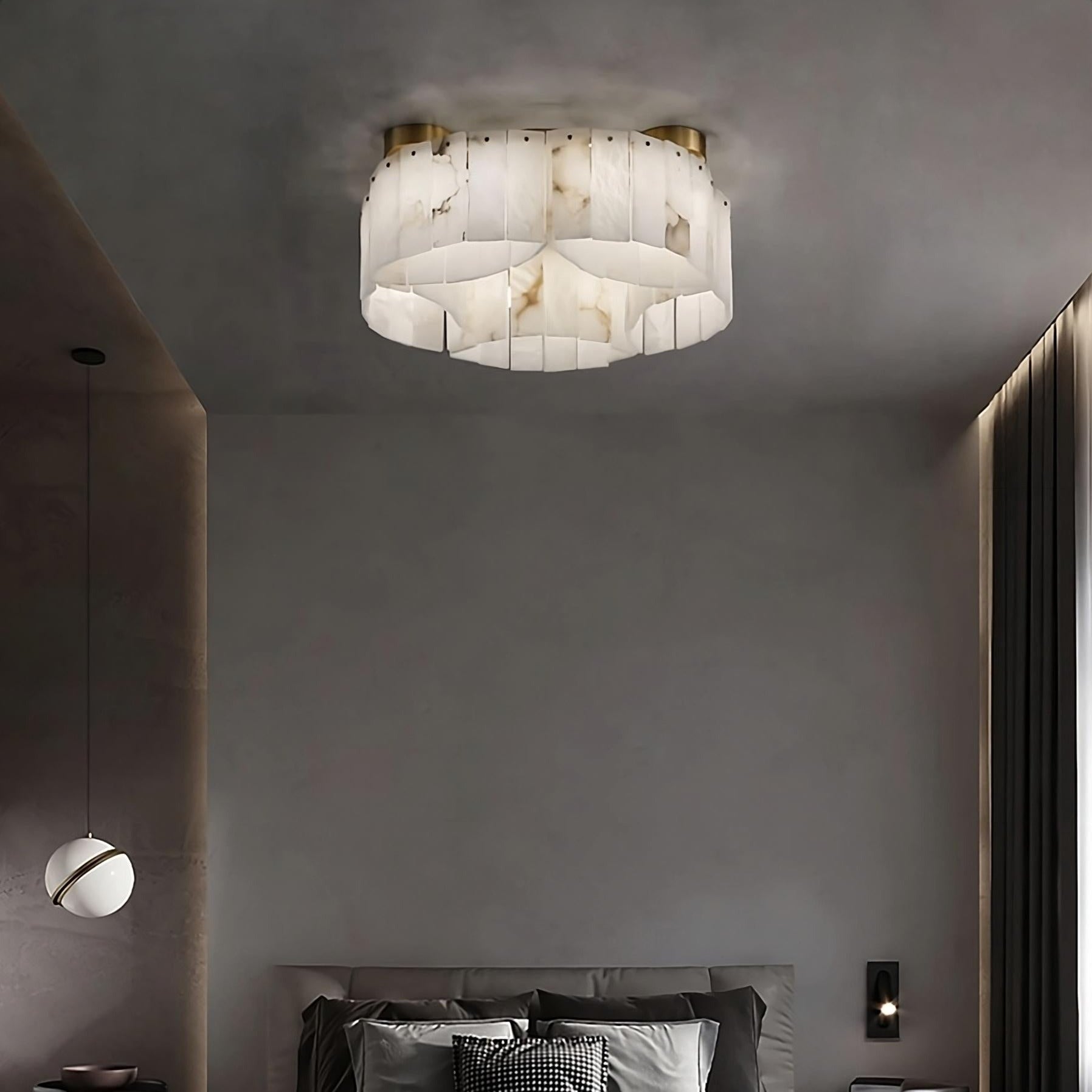 A modern bedroom featuring a large, elegant bed with gray bedding and multiple pillows. A unique, translucent Moonshade Natural Marble Ceiling Light Fixture from Morsale.com hangs from the ceiling. The room also includes minimalistic nightstands, a wall sconce, and a spherical pendant light, enhancing the modern aesthetic lighting.