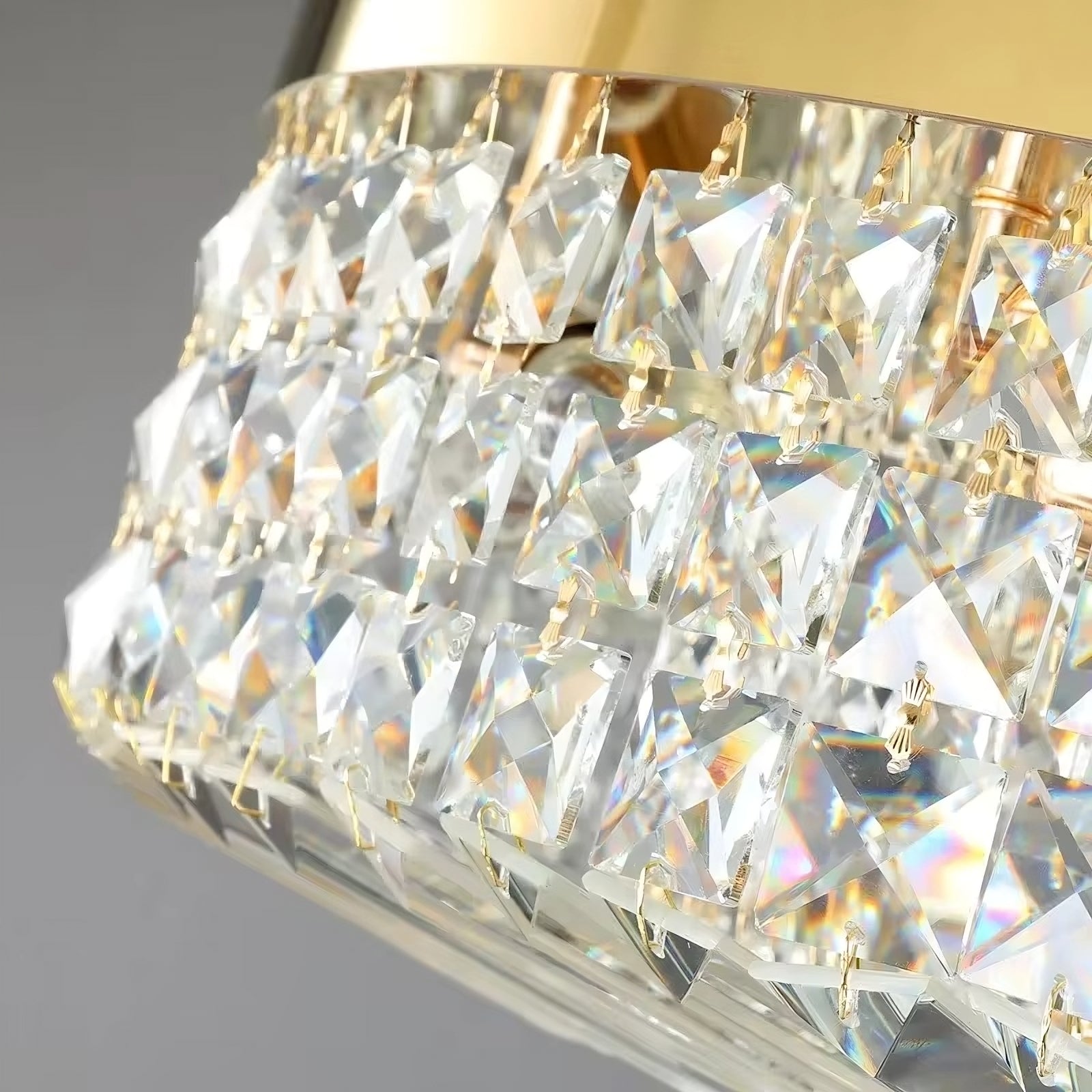 Close-up of the Gio Crystal Ceiling Light by Morsale.com, showcasing several sparkling, square-shaped crystal prisms hanging from gold fixtures. The crystal elements create a vibrant interplay of light and color reflections against a neutral gray background enhanced by LED bulbs.