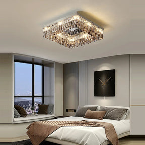 A modern bedroom features a sleek design with a large window offering a view of a distant cityscape. The centerpiece is an elegant, handmade Giano Crystal Ceiling Light by Morsale.com hanging from the ceiling. The room exudes classic luxury with its neatly made bed adorned with neutral-colored pillows and blankets.