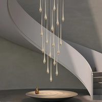 A modern interior with a spiral staircase features the Ariano Multi Pendant Chandelier from Morsale.com, teardrop-shaped gold fixtures hanging above a round minimalistic table adorned with a small golden ornament.