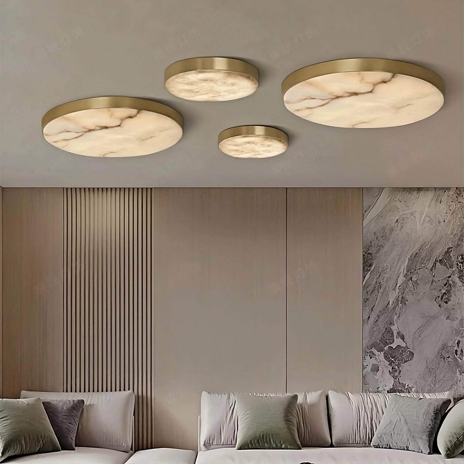 A contemporary living room highlights four Moonshade Marble & Copper Ceiling Lights by Morsale. The room includes a light-colored sectional sofa adorned with green and gray pillows, set against a textured wall featuring a marble accent panel.