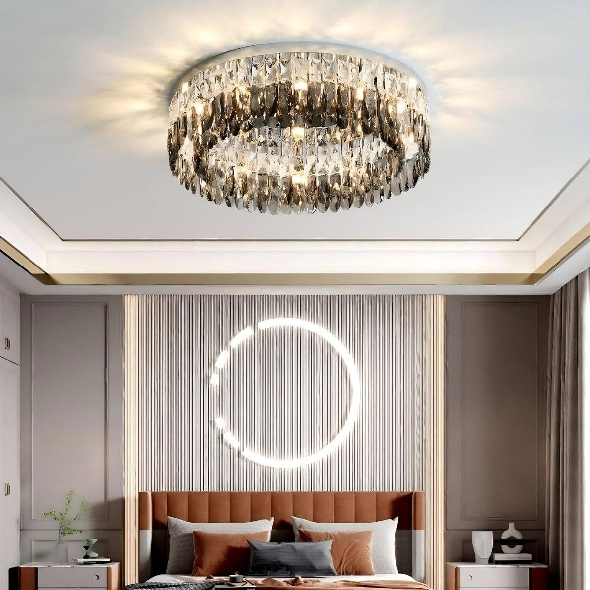 A modern bedroom features the luxurious Giano Crystal Ceiling Light Fixture from Morsale.com on the ceiling, casting warm light. The bed is adorned with rust-colored pillows and is centered against a textured, ribbed accent wall with a decorative circular light fixture. Gray cabinets flank the bed.