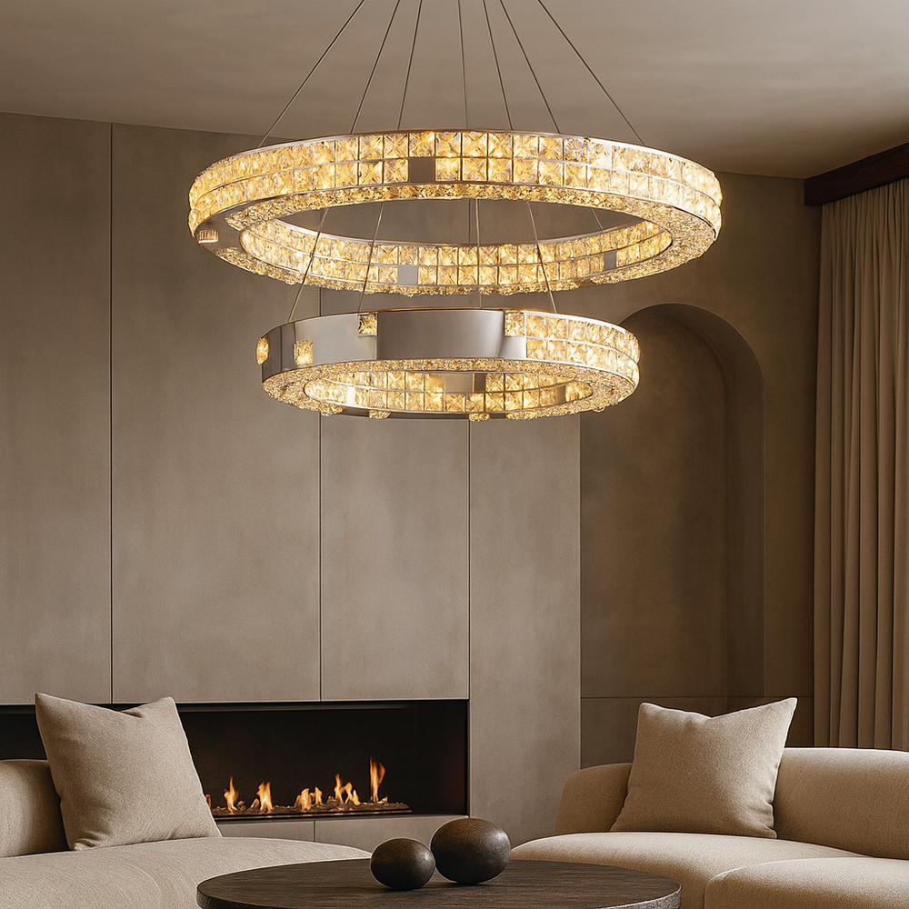 A modern living room features beige sofas, a round coffee table, a fireplace, and two Langley Modern Chandeliers by Morsale.com with LED lighting, creating a warm, elegant ambiance ideal for contemporary interiors.