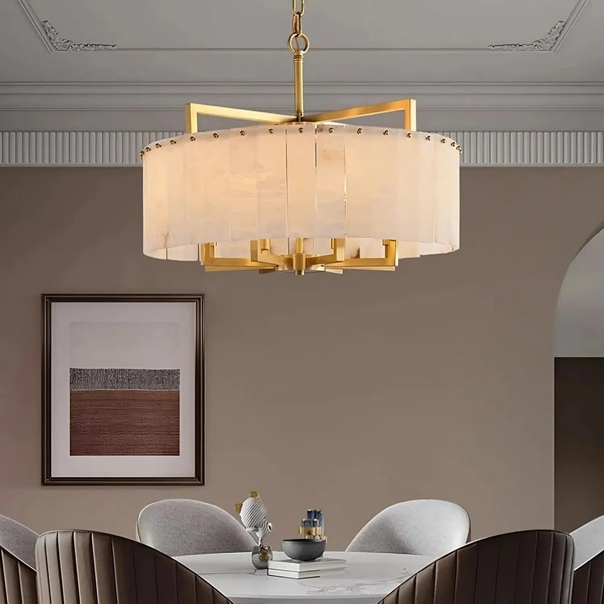 A modern dining room showcases the Morsale West Chester Marble Chandelier above a round marble table with decor and four gray chairs, while a framed abstract artwork accents the beige wall in the background.