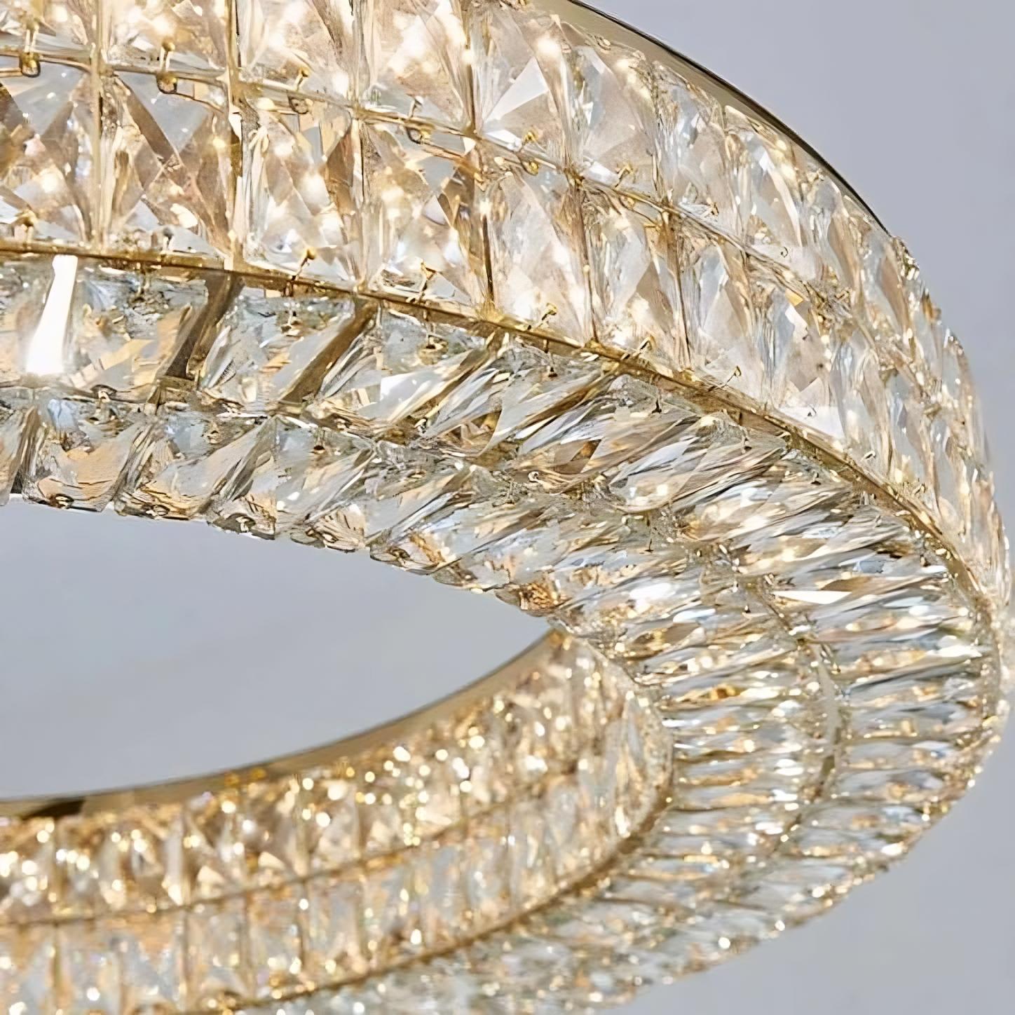 Close-up of an elegant Bacci Crystal Modern Chandelier, Gold by Morsale.com with two concentric circular rings. Each ring is adorned with numerous rectangular crystal prisms, reflecting light and creating a sparkling effect. The crystal chandelier's luxurious design stands out against a plain background.