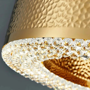 Close-up of the Morsale Alleri Hammered Gold & Crystal Chandelier, a luxurious semiflush mount light fixture. It showcases a hammered texture with a row of sparkling crystal accents that reflect light, seamlessly blending elegance and sophistication.
