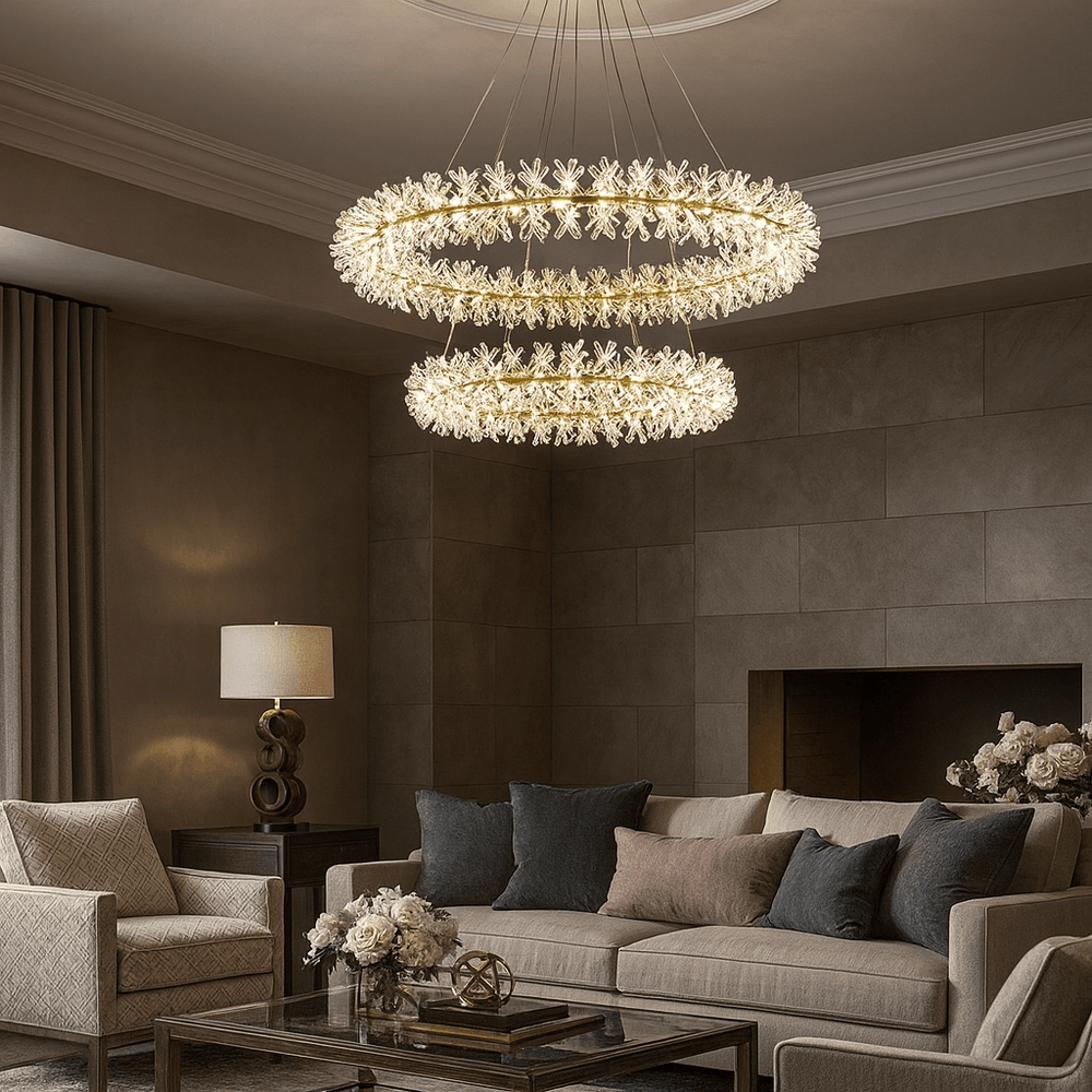A modern living room with neutral tones showcases the Exton Crystal Chandelier by Morsale.com, offering elegant mood lighting above a sofa with cushions, two armchairs, a side table with lamp, and vases of flowers for an inviting ambiance.