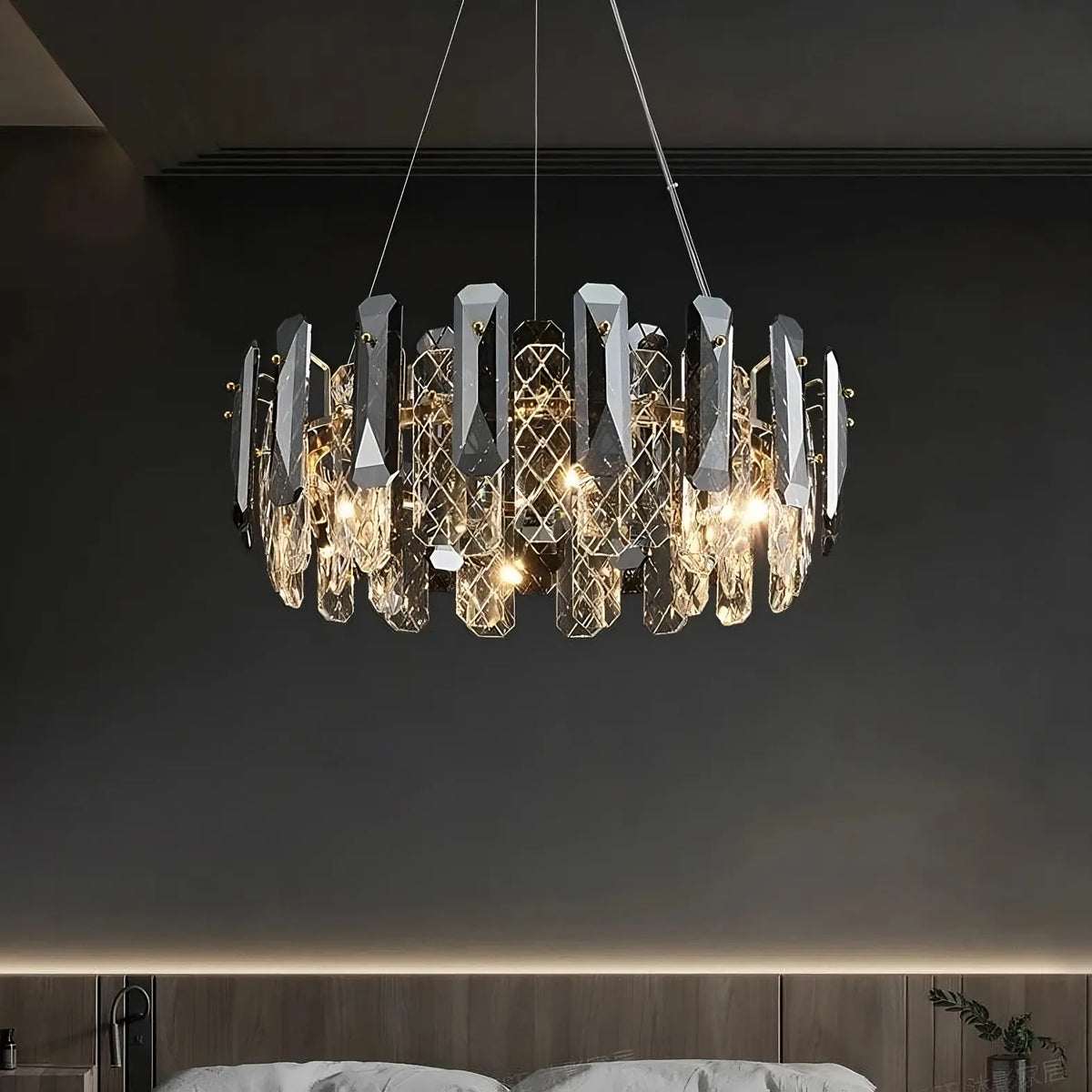 A Lazzo Crystal Ceiling Chandelier from Morsale.com, featuring geometric, crystal-like elements, hangs from the ceiling above the bed. This energy-efficient LED chandelier emits a warm light, creating a sophisticated and elegant ambiance in the room. The wall behind the bed showcases a minimalist design with subdued lighting.