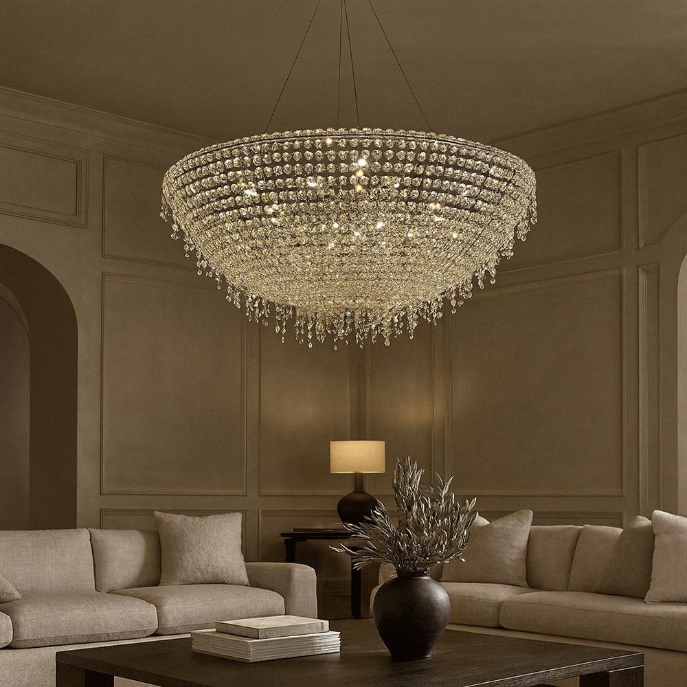 The Morsale.com Adena Crystal Tassel Chandelier graces the ceiling of a chic living room with beige walls, neutral sofas, a wooden coffee table, and a table lamp in the background.