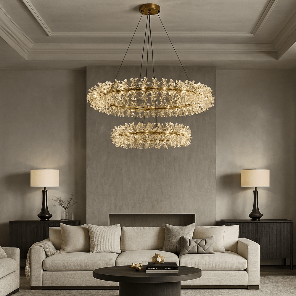 A modern living room with a beige sofa, dark wood side tables, matching table lamps, and a round black coffee table. Two Exton Crystal Chandeliers by Morsale.com hang from the ceiling, adding elegant lighting to the neutral space.