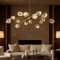 A modern living room with a cream sofa, dark coffee table, and the Diamante 15-Pendant Modern Chandelier by Morsale.com featuring multiple glass orbs, softly lit by two table lamps against a neutral stone wall and wood paneling.