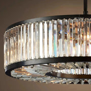 The **Gio Crystal Modern Chandelier** by **Morsale.com** is a luxurious modern chandelier with a circular design. It features rows of vertical, rectangular handmade crystals that reflect light elegantly. The crystals are framed by a sleek black metal structure and equipped with dimmable LED bulbs, creating a sophisticated and modern appearance.