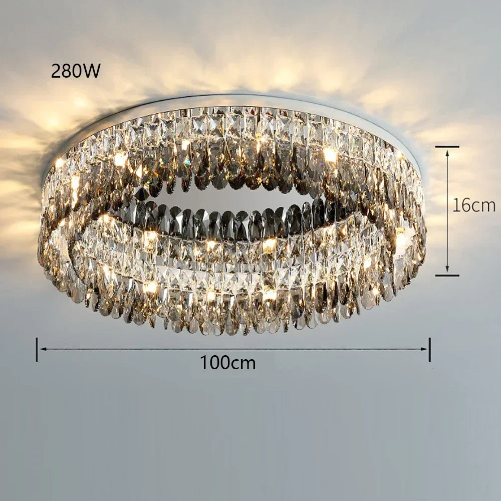 A classic luxury, Giano Crystal Ceiling Light from Morsale.com with an oval shape, hanging from the ceiling. It has a polished metal frame adorned with numerous crystal prisms that reflect light beautifully. The handmade chandelier measures 100 cm in length and 16 cm in height, and is rated at 280 watts.