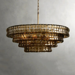 The Riviera Vintage French Crystal Chandelier by Morsale features a tiered, circular glass design with a gold metal frame and layered construction. Its textured, tinted sections emit an elegant glow against the neutral gray wall backdrop.