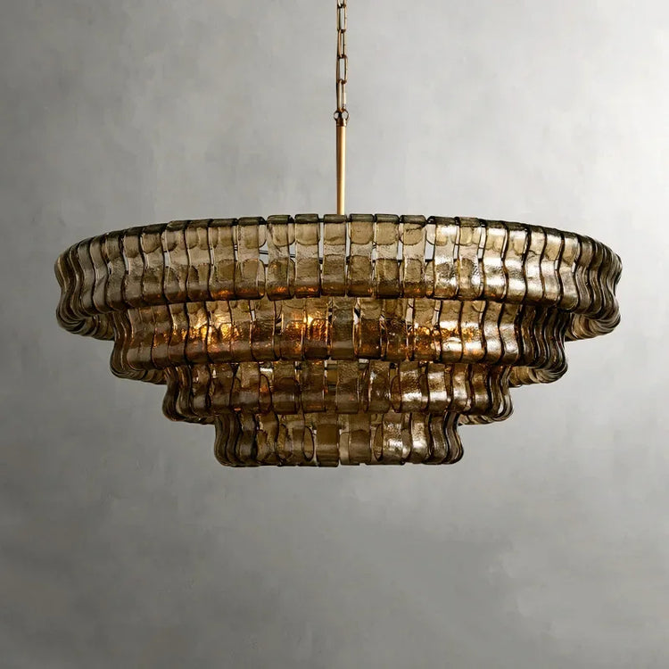 The Riviera Vintage French Crystal Chandelier by Morsale features a tiered, circular glass design with a gold metal frame and layered construction. Its textured, tinted sections emit an elegant glow against the neutral gray wall backdrop.