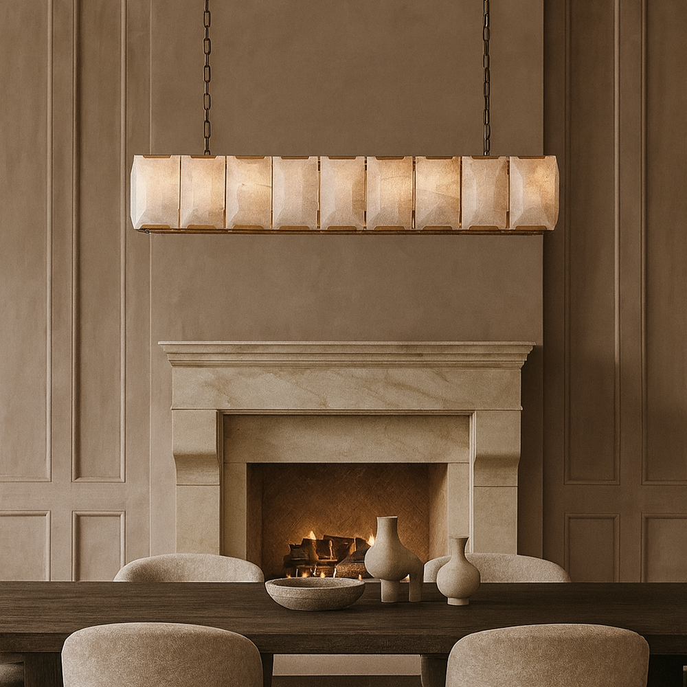 A modern, beige-toned dining room with a stone fireplace, wooden table, minimalist ceramic vases, and upholstered chairs is illuminated by the Morsale.com Brookhill Calcite Dining Chandelier, creating a warm and elegant atmosphere.