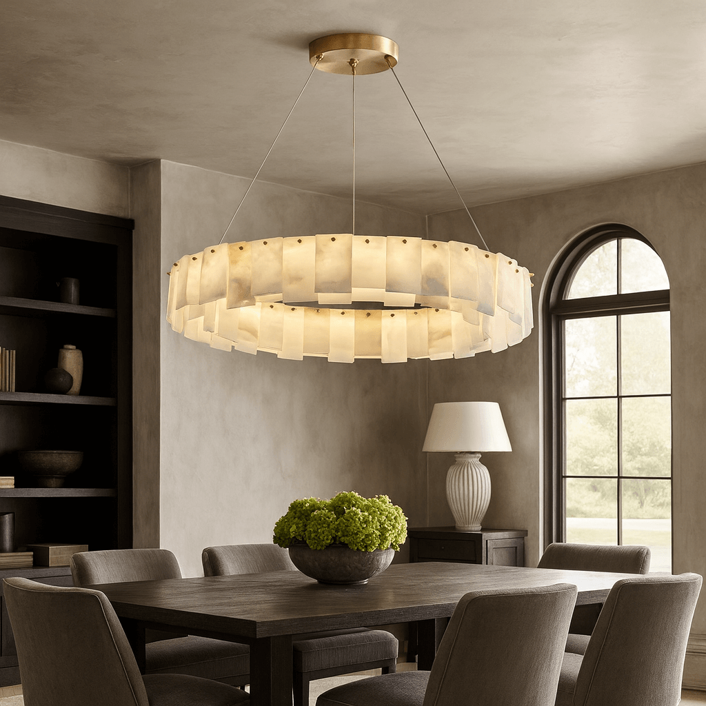 A modern dining room features the Bigman Lunaria Marble Chandelier with rectangular frosted panels, a dark wooden table, gray upholstered chairs, green flowers in a bowl, a lamp, and an arched window overlooking the garden.