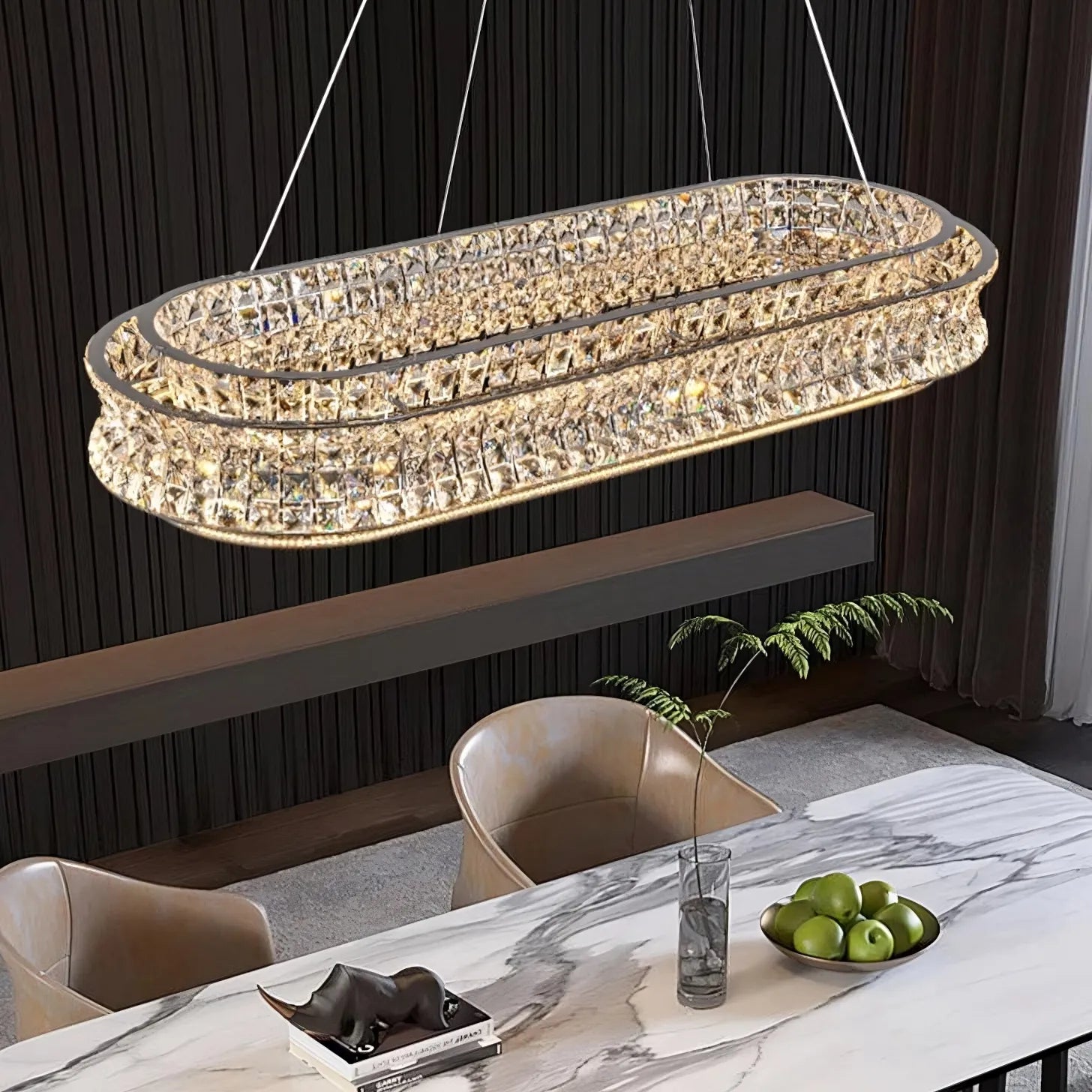 The Bacci Modern Crystal Chandelier by Morsale, with its LED lighting, illuminates a marble dining table. On the table are a bowl of green apples, a black sculpture, and a glass with a plant stem. A dark, pleated curtain in the background enhances the contemporary design.