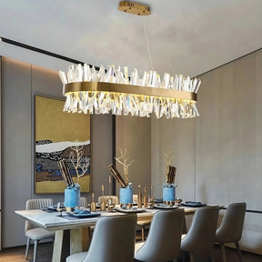 An elegant dining room features a large rectangular wooden table set for six, accompanied by chairs upholstered in soft grey fabric. Above the table, a Calvi Crystal Dining Room Chandelier from Morsale.com sparkles with K9 crystals, adding brilliance to the setting. The centerpiece is a blue vase, complemented by a large framed artwork on the wall.