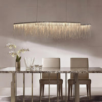 A modern dining room with a marble table, two beige chairs, white floral vase, glassware, and the 47" Cadena Metal Tassel Dining Room Light by Morsale.com as a stunning chandelier above.