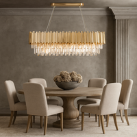 A modern dining room with a round wooden table, six beige upholstered chairs, a decorative bowl of dried flowers, and the Gio Crystal Dining Room Chandelier by Morsale.com hanging above.