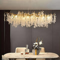 A modern dining room features a marble table, elegant chairs, a floral vase, and the Albero Frost Glass Dining Chandelier by Morsale.com, showcasing cascading white floral glass for a luxurious ambiance.