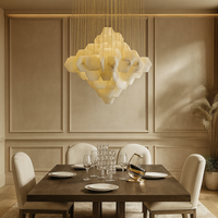 A modern dining room with a dark wood table for four, cream upholstered chairs, and beige paneled walls. The Arden Marble Pendant Chandelier by Morsale.com casts warm light above, while pampas grass in a vase accents the corner.