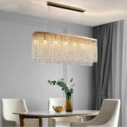 The elegant dining room features a modern centerpiece from Morsale.com: the Alleri Crystal Dining Room Chandelier, crafted from handmade crystals. Two white chairs complement the table with greenery and a golden bowl, while gray curtains enhance the sleek decor.