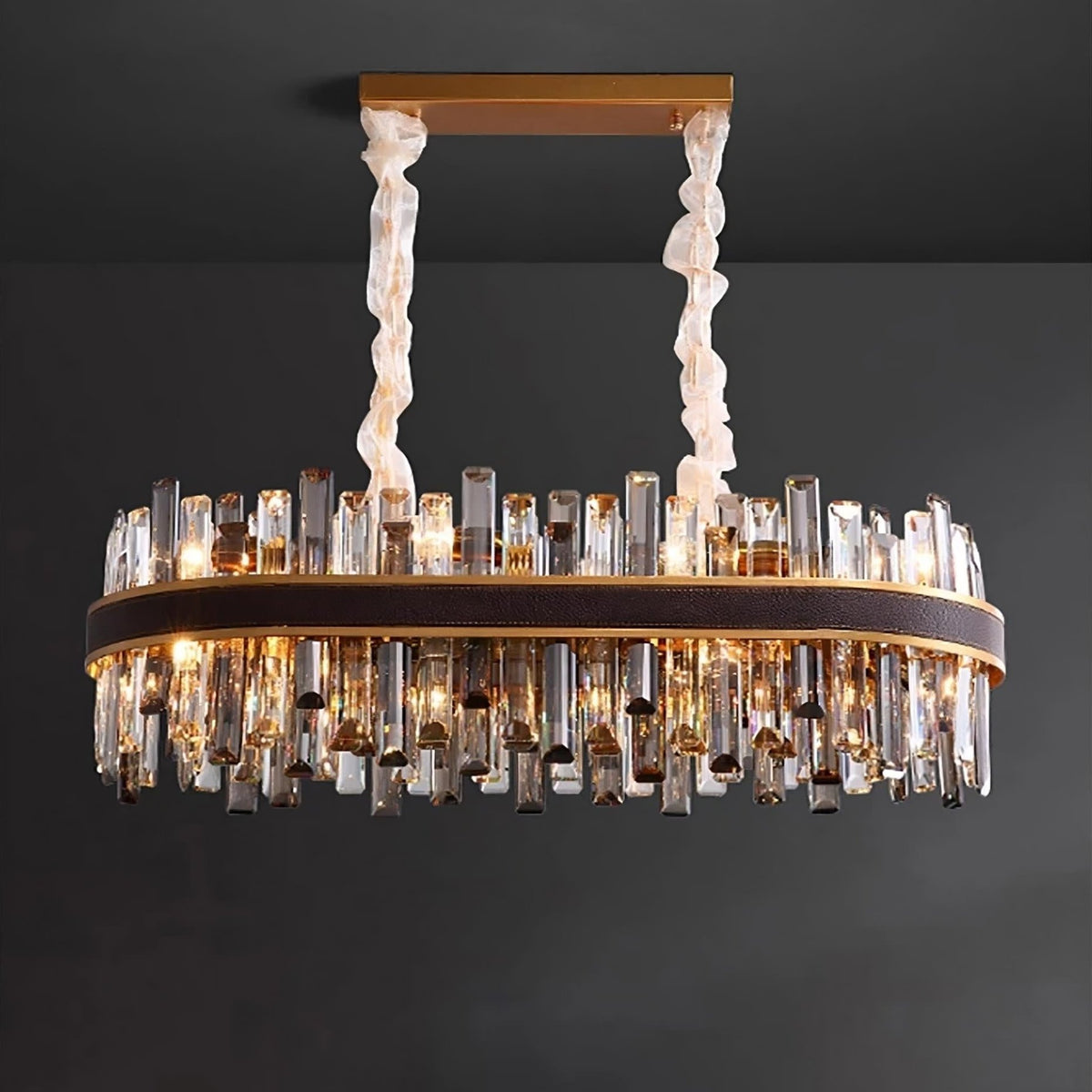 The Calvi Crystal Dining Room Chandelier from Morsale.com lights up, casting a warm glow with its premium crystals and golden frame. The rectangular fixture is suspended from a golden bar attached to the ceiling using two decorative fabric-wrapped cords. The text "lights on" is displayed at the bottom.