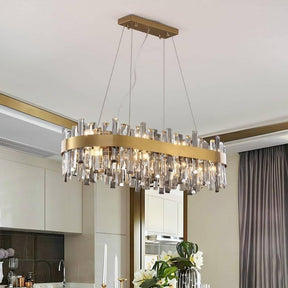 The Asti Dining Room Chandelier by Morsale.com, featuring a modern gold rectangular design with dangling clear crystal accents, hangs gracefully from the ceiling. It casts a warm light over a white floral arrangement on the dining table. The room is adorned with neutral-toned walls, stainless steel curtains, and a reflective mirror.