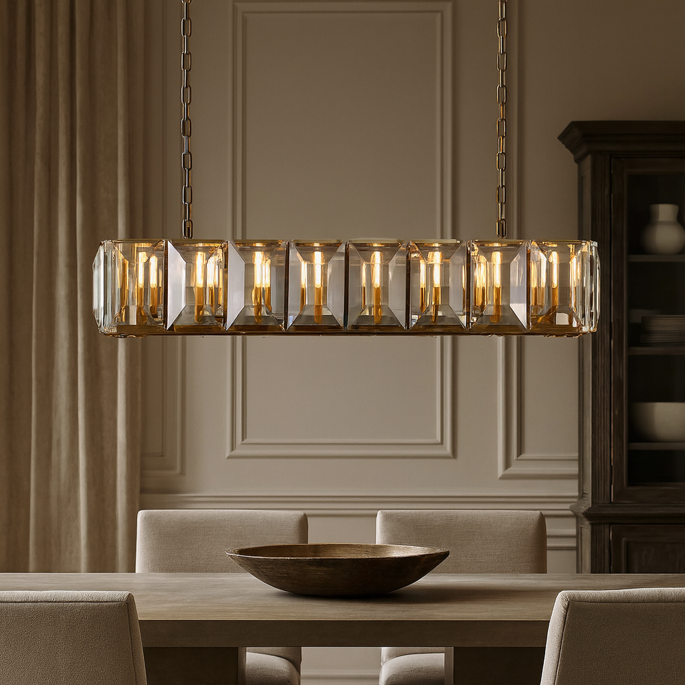 The Brookhill Crystal Dining Chandelier from Morsale.com casts warm light above a modern dining table with beige chairs and a wooden bowl, in an elegant room featuring paneled walls and floor-length curtains.