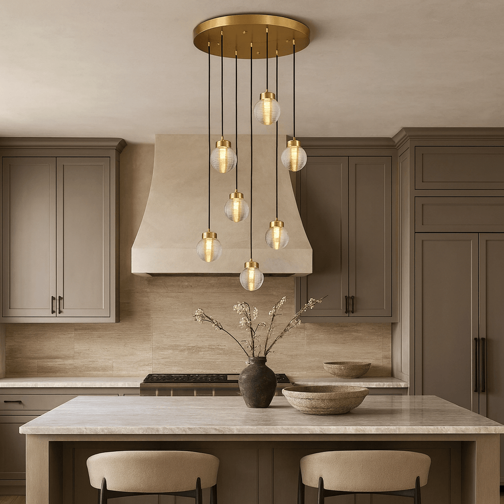 
                  
                    Modern kitchen with taupe cabinets, marble island, two beige stools, and a Morsale Bossen 7-Globe Chandelier overhead. A vase with branches and two bowls sit atop the island.
                  
                