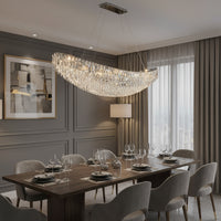 A modern dining room with a large wooden table, surrounded by plush beige and grey chairs. Above the table hangs a striking Gio Crystal Dining Room Light Fixture by Morsale.com with multiple lights, suspended by thin wires. The background features a dark grey wall and tall curtains, creating a perfect setting for modern home lighting.