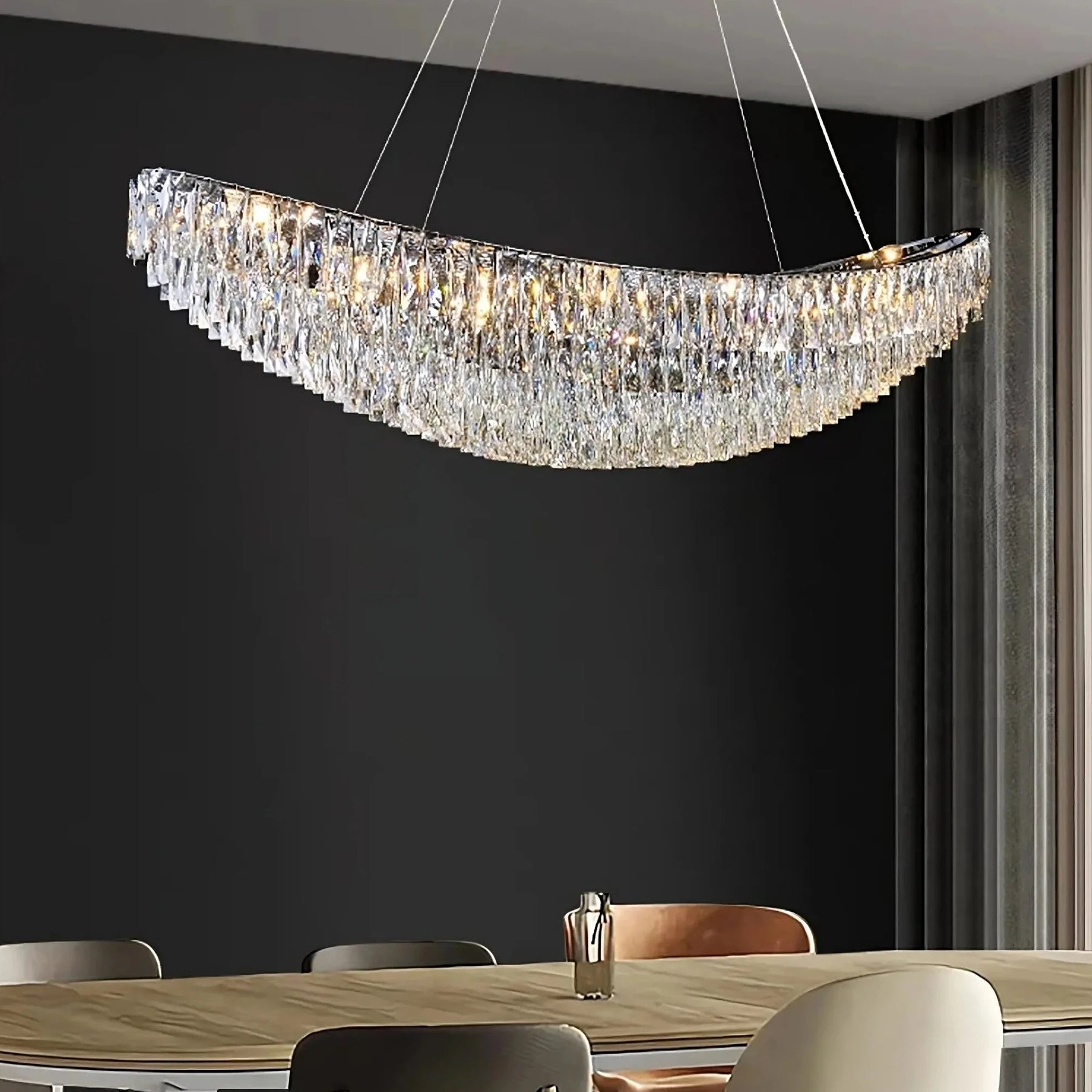 A modern dining room with a large wooden table, surrounded by plush beige and grey chairs. Above the table hangs a striking Gio Crystal Dining Room Light Fixture by Morsale.com with multiple lights, suspended by thin wires. The background features a dark grey wall and tall curtains, creating a perfect setting for modern home lighting.