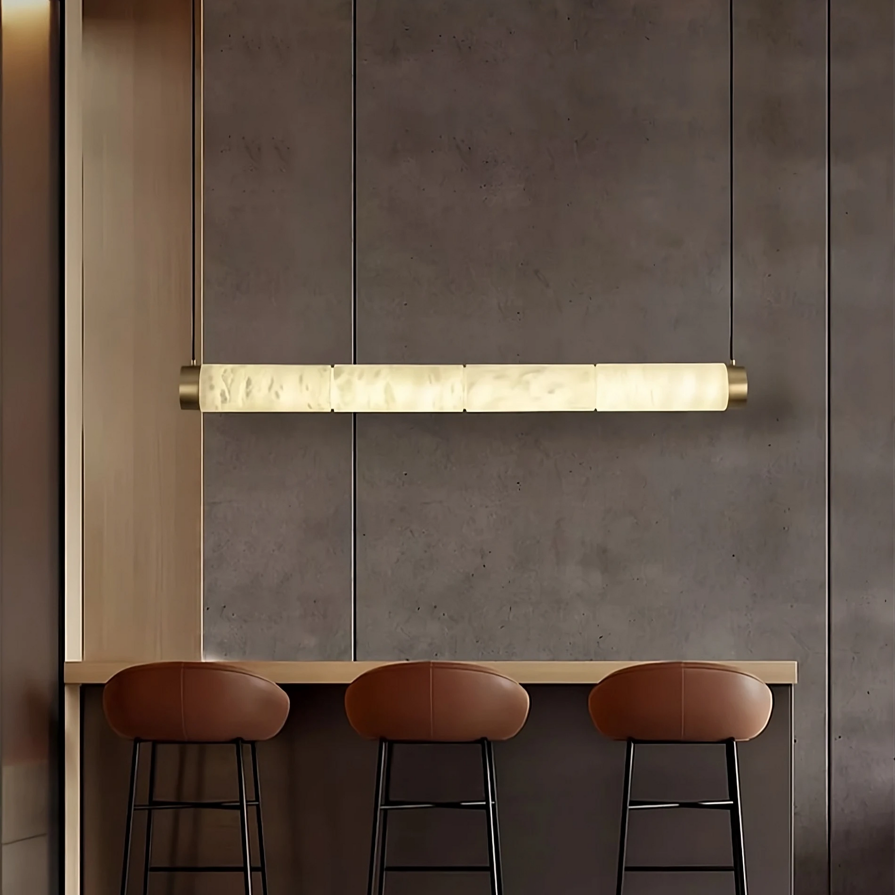 A modern, minimalist bar area features three brown leather barstools lined up against a sleek, dark countertop. Above the countertop hangs an elegant Bigman Moonshade Natural Marble Dining Room Light Fixture. The background boasts a smooth, dark wall surface, enhancing the sophisticated ambiance.