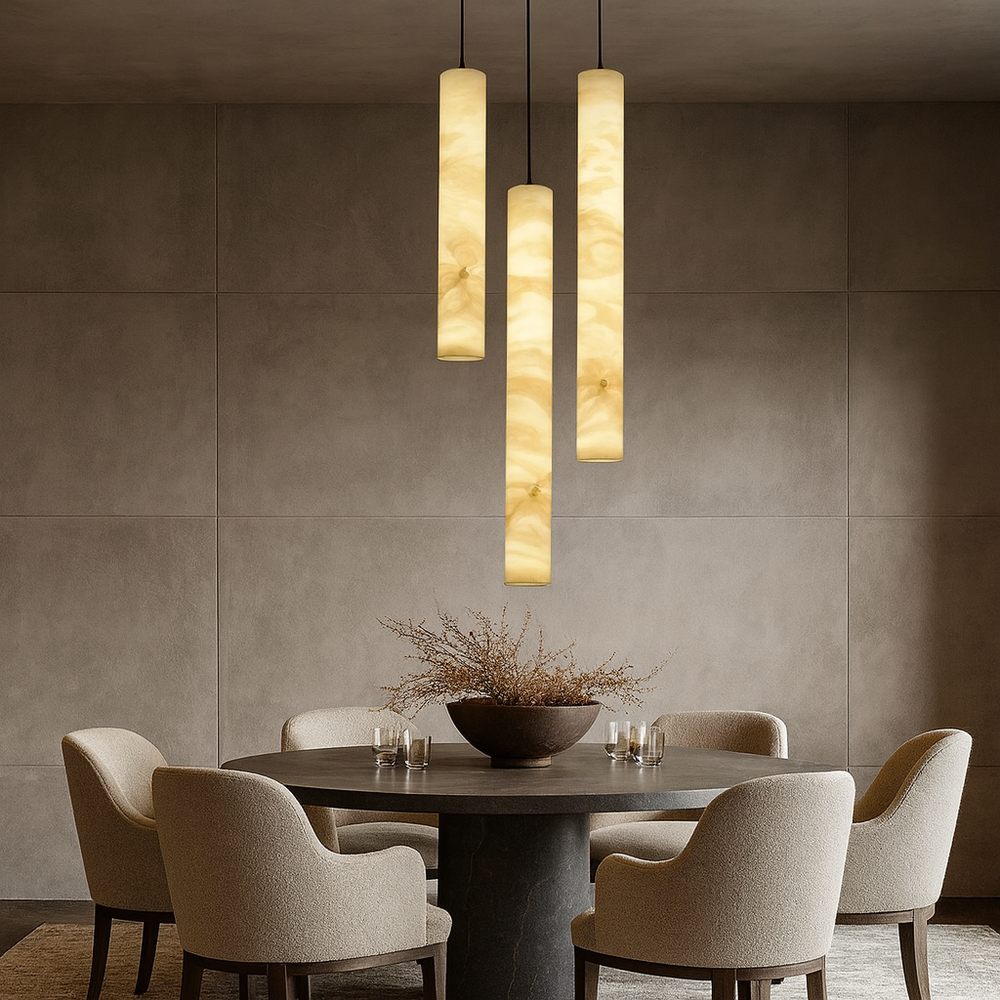 
                  
                    A modern dining room featuring a round table, five upholstered chairs, a dried floral centerpiece, and four Morsale Moonshade Marble Pendant Lights hanging above, set against textured taupe wall panels.
                  
                